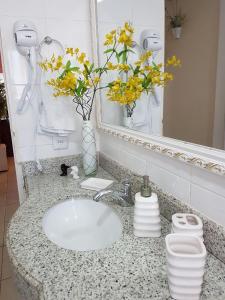 a bathroom sink with a vase with yellow flowers on it at Geriba Apart Hotel in Búzios