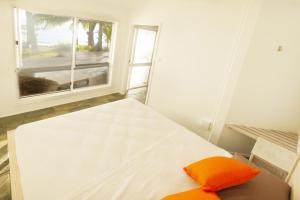 a bed with an orange pillow in a room with a window at Drift Beach House Getaway in Holloways Beach