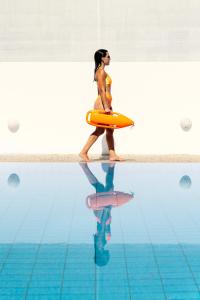a woman in a bathing suit walking next to a swimming pool at Coralli Seaside Resort in Livadakia
