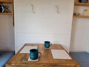 dos tazas de café sentadas en una mesa de madera en The Shepherds Hut at Forestview Farm en Greenisland