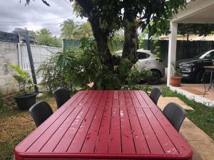 une table rouge avec des chaises et un arbre dans une cour dans l'établissement Meublé le manguier, à Saint-Pierre