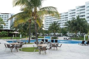 a palm tree with tables and chairs next to a pool at Villa Magna departamento en Nuevo Vallarta in Nuevo Vallarta 