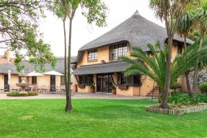 a house with a thatched roof and palm trees at Hotel Nomad Belvedere Lodge in Midrand