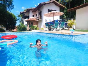 a young girl is swimming in a swimming pool at Casa da Cocanha COND com PISCINA-SINUCA-CHURRASQ-DECK com vista para o mar in Caraguatatuba