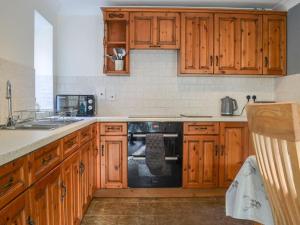 a kitchen with wooden cabinets and a black dishwasher at Rose Cottage - Uk41345 in Cromer