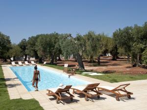 a woman walking next to a swimming pool with chairs at I Mulicchi in Specchia