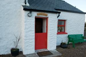 a white building with a red door and a green bench at Cobblers Cottage Creggan in Greencastle