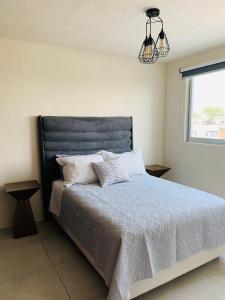 1 dormitorio con 1 cama con cabecero azul y ventana en Departamento nuevo y céntrico con ambiente familiar en Guadalajara, en Guadalajara