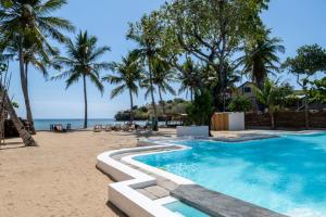 una piscina junto a una playa con palmeras en Swisscocobeach, en Nosy Be