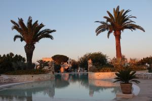 a swimming pool with palm trees in a resort at Masseria Valente in Ostuni