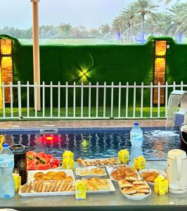 a table with plates of food next to a swimming pool at شالية البندرvip in Ḩifrī