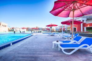 Porto Sharm Hotel Apartments Delmar for touristic investment في شرم الشيخ: مجموعة كراسي ومظلات بجانب مسبح