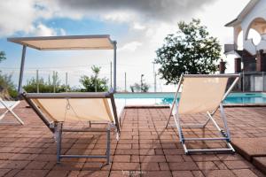 twee stoelen en een parasol naast een zwembad bij Tenuta Carbone - Con piscina e parcheggio privato in Mascali