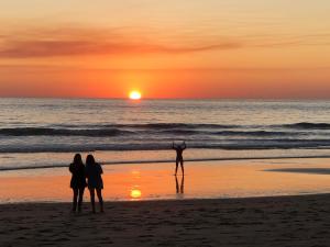 un grupo de personas de pie en la playa al atardecer en Casa a 65 metros de la Playa en El Palmar