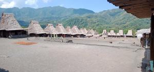 a group of straw umbrellas on a beach with mountains at Kristian Homestay in Bajawa