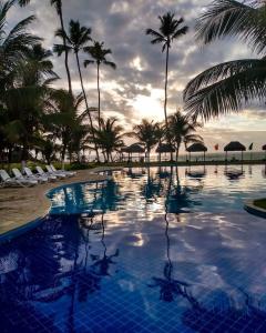 a swimming pool with palm trees and a cloudy sky at Ancorar flat resort paradise in Porto De Galinhas