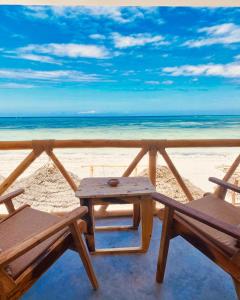 Helwas Zanzibar Beach Hotel في بويجو: طاولة نزهة وكرسيين على الشاطئ
