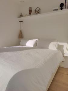 uma cama branca com lençóis brancos e almofadas em La Naturale Garden zeezicht em Zeebrugge
