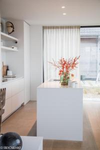 a white kitchen with a vase of flowers on a counter at La Naturale Garden zeezicht in Zeebrugge +24 photos