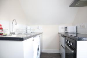 a white kitchen with a sink and a dishwasher at Twelve Thirty Serviced Apartments - 1 Croydon in South Norwood