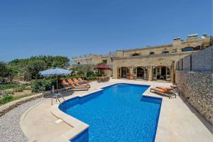 a swimming pool with chairs and an umbrella next to a building at The Olives Holiday Home in San Lawrenz