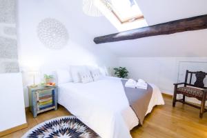 a white bedroom with a bed and a chair at Vella Nova by Serendipia Turismo in Santiago de Compostela