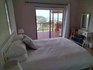 1 dormitorio con cama blanca y balcón en 2 Bedroom Guest Suite at A-frame Glengariff Beach en Glen Eden