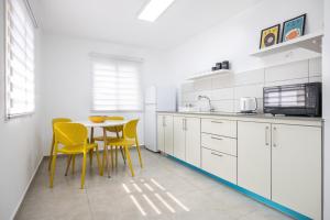 a white kitchen with yellow chairs and a table at אירוח פינת חן - מתחם אירוח מושלם עם בריכה משותפת in Ramot Naftali