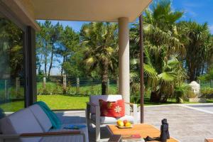 un porche con una silla blanca, una mesa y algunas palmeras en Villa Montalvo, en Sanxenxo