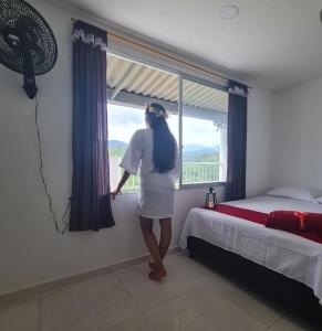 a woman standing in a bedroom looking out the window at MIRADORES D ALESSANDRA in Pueblo Bello