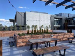 um pátio com duas mesas de piquenique e uma parede de tijolos em Modern new 1-bedroom apartment in Canberra City em Camberra