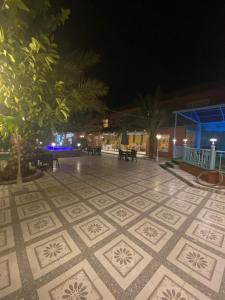 un patio de azulejos por la noche con mesas y árboles en فندق ادوماتو ADOMATo HOTEl, en Dawmat al Jandal