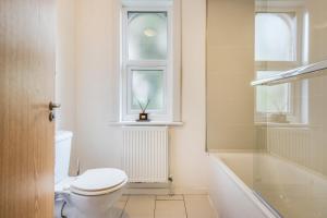 a white bathroom with a toilet and a window at Apartments in Brixton next door to Brockwell Park in London