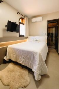 1 dormitorio con 1 cama blanca y TV en la pared en Malbec Casa Hotel, en Bento Gonçalves