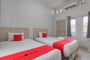2 camas en una habitación de hotel con almohadas rojas en RedDoorz Plus Syariah @ Tuparev Cirebon 3 en Cirebon