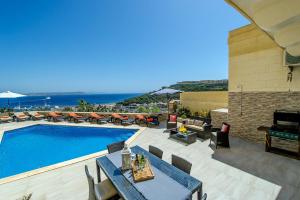 una piscina con mesas y sillas junto a un edificio en The Harbour Holiday Home en Għajnsielem