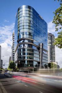 a tall glass building with cars in front of it at Adina Apartment Hotel Melbourne Southbank in Melbourne