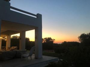 eine Terrasse mit einem Stuhl und einem Sonnenuntergang im Hintergrund in der Unterkunft Villa Agosto, luxe villa met zwembad en zeezicht in Puglia in Carovigno