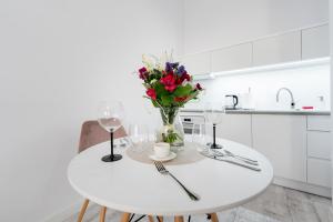 a white table with a vase of flowers and wine glasses at Apartamenty Centrum nowoczesny design - Dream Apart in Bielsko-Biala
