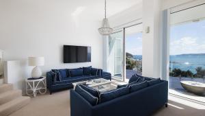 a living room with blue furniture and a large window at Riviera - Panoramic Water Views In The Heart Of Nelson Bay in Nelson Bay