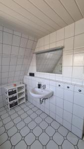 a white tiled bathroom with a sink and a mirror at Ferienhaus Hoddebüll nah an der Nordsee in Emmelsbüll-Horsbüll