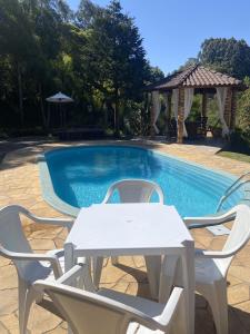 een witte tafel en stoelen naast een zwembad bij Sítio dos Coqueiros, em meio a natureza com piscina in Carlos Barbosa