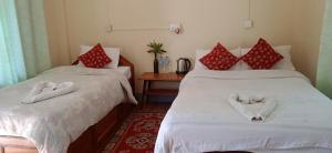 a room with two beds with white sheets and red pillows at Crocodile Safari Camp in Chitwan