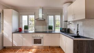 una cocina con armarios blancos, fregadero y ventanas en Villa de los Sueños Atarfe by Ruralidays en Atarfe