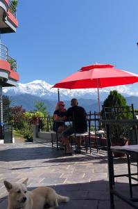 twee mensen zitten aan een tafel onder een paraplu met een hond bij Hotel Pristine Himalaya in Pokhara