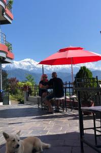 two people sitting at a table under an umbrella with a dog at Hotel Pristine Himalaya in Pokhara