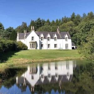 a large white house with its reflection in the water at St Marys Farmhouse - Traditional Country Farmhouse with Open Fire in Fochabers
