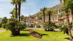 un complexe avec des palmiers et une montagne en arrière-plan dans l'établissement Hotel Du Lac, à Locarno