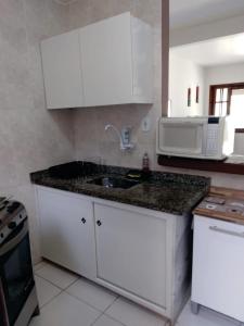a kitchen with white cabinets and a sink and a microwave at Uma PAUSA na sua vida, com: sol, praia e sossego! in Cabo Frio