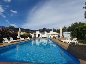 a swimming pool with chairs and umbrellas in front of a house at Brydar with Sauna, Swimming Pool and Jacuzzi in Mielno